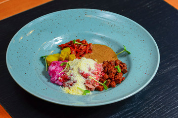Vegetable salad with sause served on a blue plate on dark rustic wooden table in restaurant.