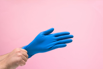 medical blue glove on the man's hand from the coronavirus on a pink background. space for text. protecting the body from viruses and bacteria
