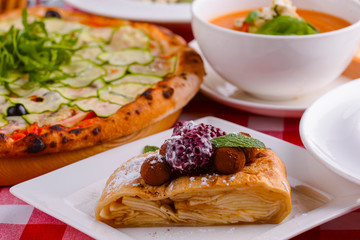Cake of puff pastry with raspberry and chocolate served on a white plate with other Italian dishes on a table.