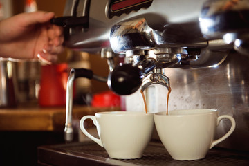 Fototapeta premium Close up of espresso pouring from coffee machine in two white cup. Professional cappuccino brewing