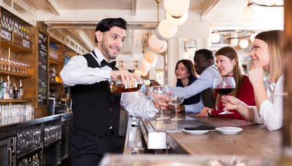 Portrait of young barman and people who are standing near bar counter