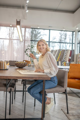 Joyful woman sitting at a table in a large bright room.