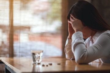 Closeup image of a headache woman with white pills and a glass of water on the table