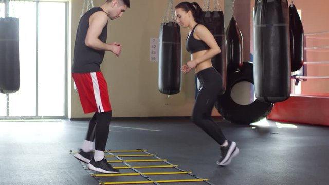 Male and female boxers exercising with double agility ladder while training together in gym