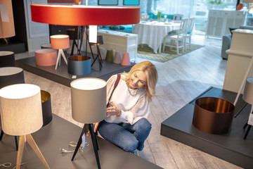 Woman crouched near a beige floor lamp.