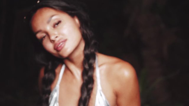 Cute and sexy brunette girl in silver bikini top, denim shorts and sunglasses dancing, smiling, flirting during summer evening - video in slow motion