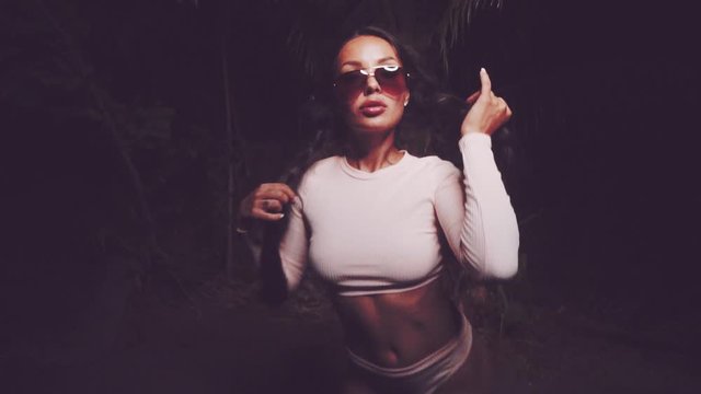Cute and sexy brunette girl wearing pink long sleeve crop top and panties set and sunglasses dancing, smiling, flirting during summer evening - video in slow motion