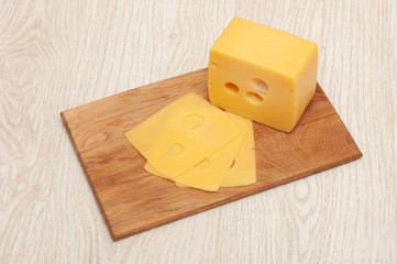 Piece of cheese and sliced cheese on a wooden board