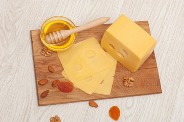 Piece of cheese and sliced cheese on a wooden board with honey, nuts and dried apricots. Top view