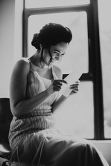 Caucasian bride reading emotional a letter written by her groom. Beautiful lady in a bright room on a chair. 