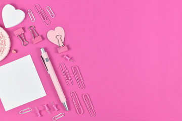 Flat lay with various arranged stationery supplies like pen, note paper, pins or retaining clip on pink background with blank copy space on right side