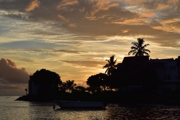 Colorful tropical sunset through coconut palm trees, villa and beautiful bay of water. © Christophe