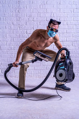 Athletic man in a medical mask and glasses vacuums a room.