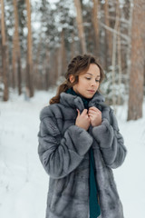 a beautiful girl in a wedding dress stands in a winter pine forest