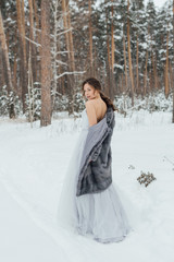 Fototapeta na wymiar a beautiful girl in a wedding dress stands in a winter pine forest