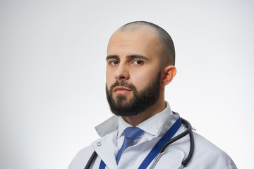 A close portrait of a serious doctor with a beard. A physician practitioner in a white lab coat, a blue tie, and a stethoscope.