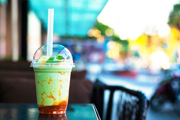 Close-up transparent glass with ice cream, green tea and caramel. Milkshake decorated with mint and fruit in a coffee shop on the terrace, outdoors