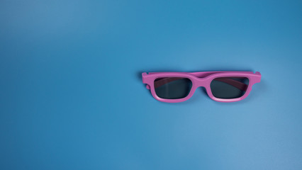 Pink 3D glasses for watching a movie on a blue background. Flatlay