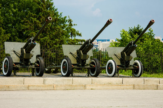 Three old cannons on a pedestal against a background of green trees