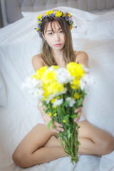 Sexy Asian woman in lingerie, holding a bouquet of flowers, sitting relax on her bed