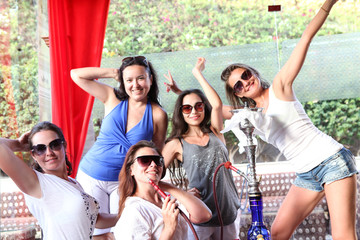 The company of young beautiful girls smokes a hookah. Smoke. The girl releases smoke. Tobacco.