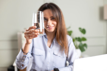 Close up of woman holding glass of water while using laptop.