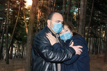 A sad adult couple, a man and a woman in medical masks embrace in the forest. Concept of a pandemic...