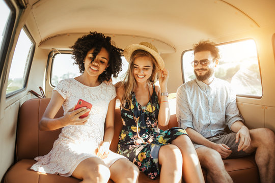 Three Best Friends Travel In A Minivan Bus And Explore New Places. Two Girls And One Boy Having Good Times. Taking Pictures And Selifies. Hugging And Kissing Eachother