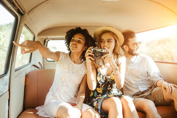 Three best friends travel in a minivan bus and explore new places. Two girls and one boy having good times. Taking pictures and selifies. Hugging and kissing eachother