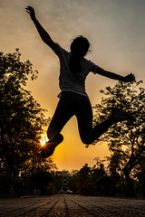 A Silhouette picture of a woman jumping in joy on the road with a sunset background