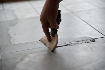 Tiler laying the ceramic tile on the floor. Professional worker makes renovation. Construction. Hands of the tiler. Home renovation and building new house - obrazy, fototapety, plakaty