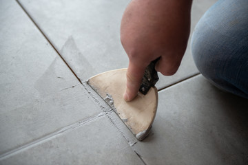 Tiler laying the ceramic tile on the floor. Professional worker makes renovation. Construction. Hands of the tiler. Home renovation and building new house - obrazy, fototapety, plakaty