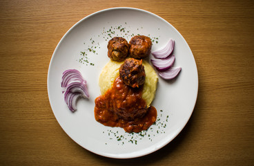 Mashed potato with meatballs in tomato sauce on white plate on wooden background