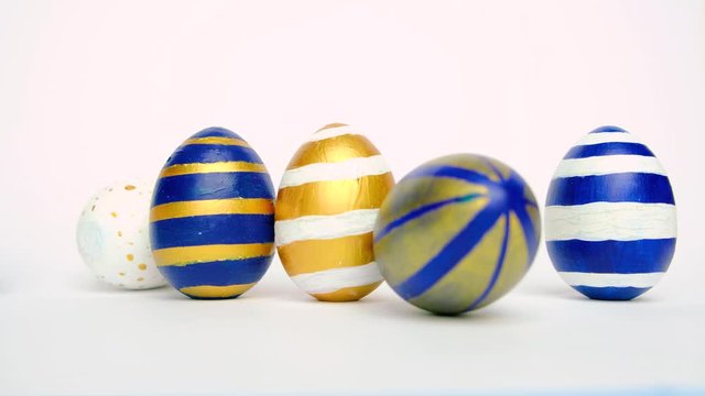 Easter eggs are rolling, knocking each other on white table. Eggs trendy colored classic blue, white and golden . Happy Easter. Minimal style