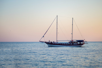 Fototapeta na wymiar Beautiful small pleasure cruise ship with masts sailing at sunset
