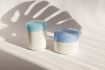 White blank mockup of bottle cream containers with blue cups. Monstera shadows. Professional tubes for facial and body treatment.