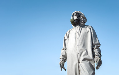A man in a gas mask and a protective suit. Blue sky in the background. With copyspace