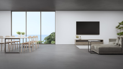 Table on concrete floor of bright dining room near large living room and sofa against TV in modern beach house or luxury hotel. Minimal home interior 3d rendering with sea view.