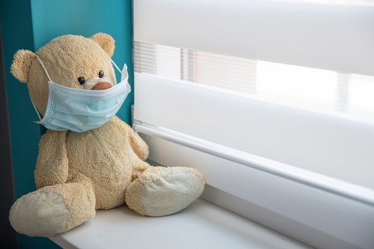 Bear mascot on the windowsill of a hospital window in a medical mask.