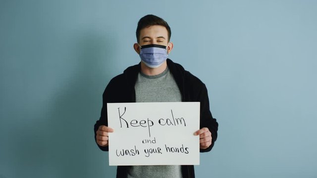 Young man in protective mask is holding a poster, urging others to keep calm during the coronavirus pandemic and follow hygiene recommendations, health and safety concept.