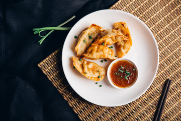 Asian dumplings Gyozas potstickers fried on cast-iron pan, served with chopsticks and bowl of soy sesame sauce over black texture background. Top view, space...N.