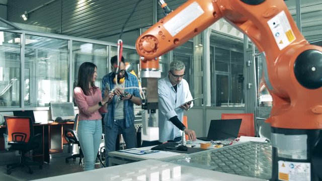 Robotic arm is moving and the students are observing bionic elements. Young engineers working in innovative laboratory.