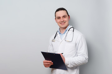 portrait of a young smiled doctor in a dressing gown, with a stethoscope and a clipboard.