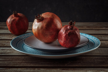 Ripe pomegranates in a plate on a wooden background. Still life.