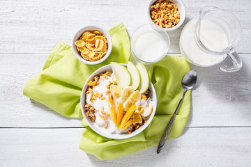 Granola and vegetarian yogurt with slices of apple, apricot, banana and a jug of milk on a white wooden background. Healthy breakfast concept. Top view
