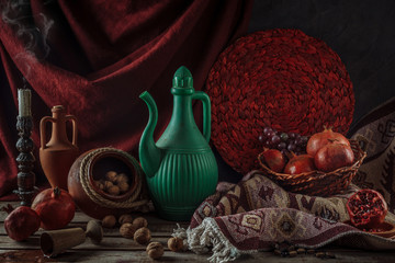 Still life with pomegranates and walnuts. Oriental flavor. Horizontal format. Ceramic jugs with wine.