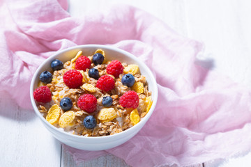 Bowl with granola, blueberries and raspberries and pink cloth on a white background. Healthy breakfast concept