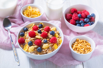 Yogurt, bowls with granola, blueberries and raspberries, cornflakes and puffed rice on a white wooden background. Healthy breakfast