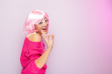 Caucasian woman with pink wig and sweater, wearing white glasses, posing funny at the photo studio. Funny expressive women and colorful portrait concept. Pink.