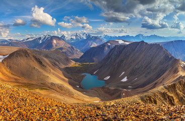 Mountain view. Turquoise lake deep in the valley. Snow-capped peaks and picturesque sky.